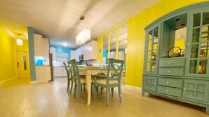 Un coin repas avec une table et des chaises en bois, un buffet bleu et, au fond, une cuisine.