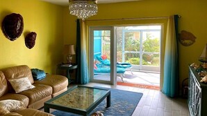 Un salon comprenant un canapé, une table basse et donnant sur un espace extérieur où se trouve une chaise bleue.