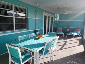 Un patio couvert comprenant une table et des chaises, un ventilateur de plafond et une porte donnant sur un espace extérieur.