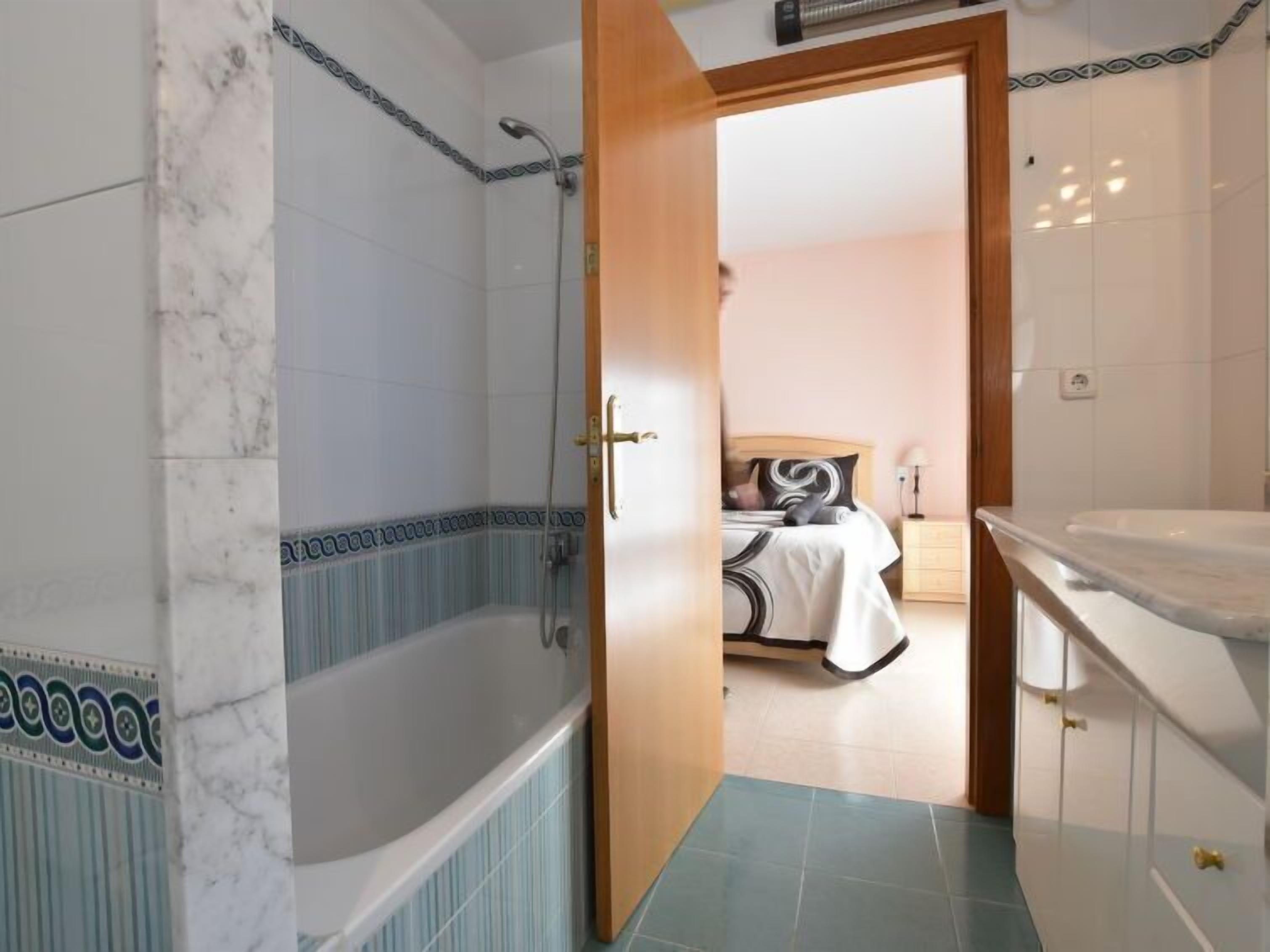 Ein Badezimmer mit Badewanne, Dusche und einer Tür zu einem Schlafzimmer mit Bett und Nachttisch.