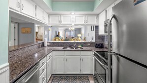 A kitchen with white cabinets, granite countertops, a stainless steel refrigerator, and a patterned rug. - Enjoy the breeze from the screened in porch on summer nights at Summertree Villa (Myrtle Beach)
