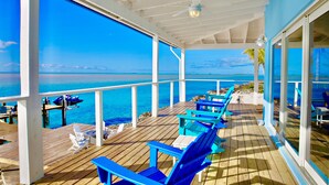 A covered deck with blue chairs and tables, overlooking a clear blue sea. - Great Location,  beautiful home on the water,beach, pool and top amenities (Georgetown)