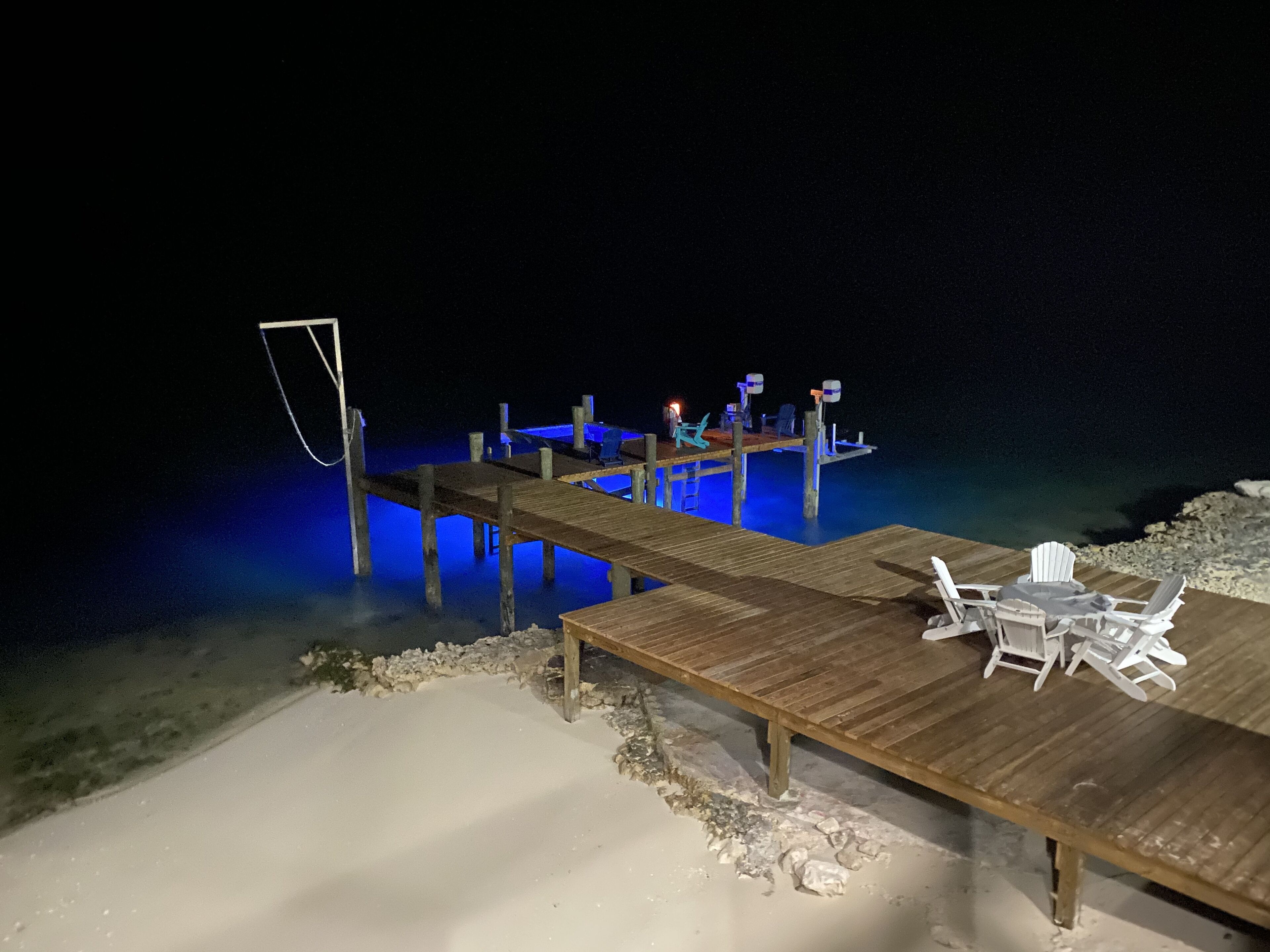 A wooden deck extending into a body of water, with a table and chairs set up for dining.