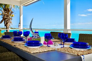 A dining table set with blue dinnerware and wine glasses, overlooking a clear blue ocean. - Great Location,  beautiful home on the water,beach, pool and top amenities (Georgetown)