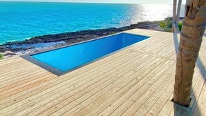 A wooden deck with a rectangular pool overlooking a turquoise sea. - Great Location,  beautiful home on the water,beach, pool and top amenities (Georgetown)