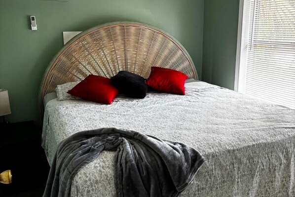 A bed with a woven headboard, a grey blanket, and red and black pillows.