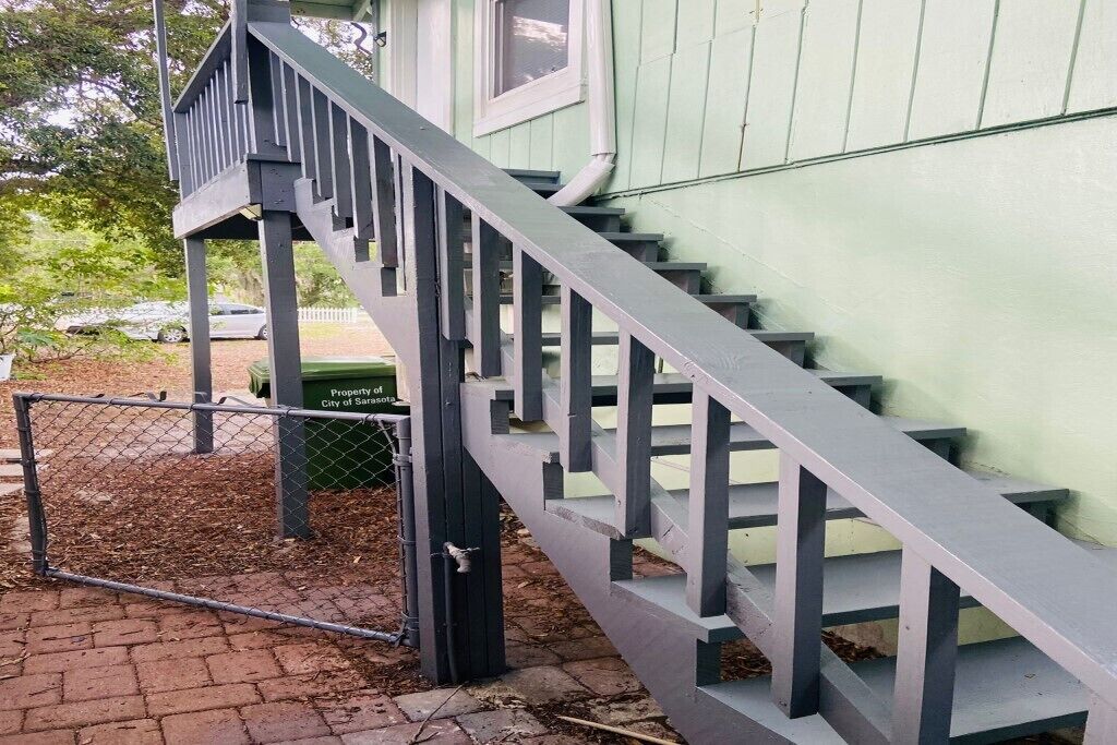 A staircase leading to a green building with a metal fence in front.