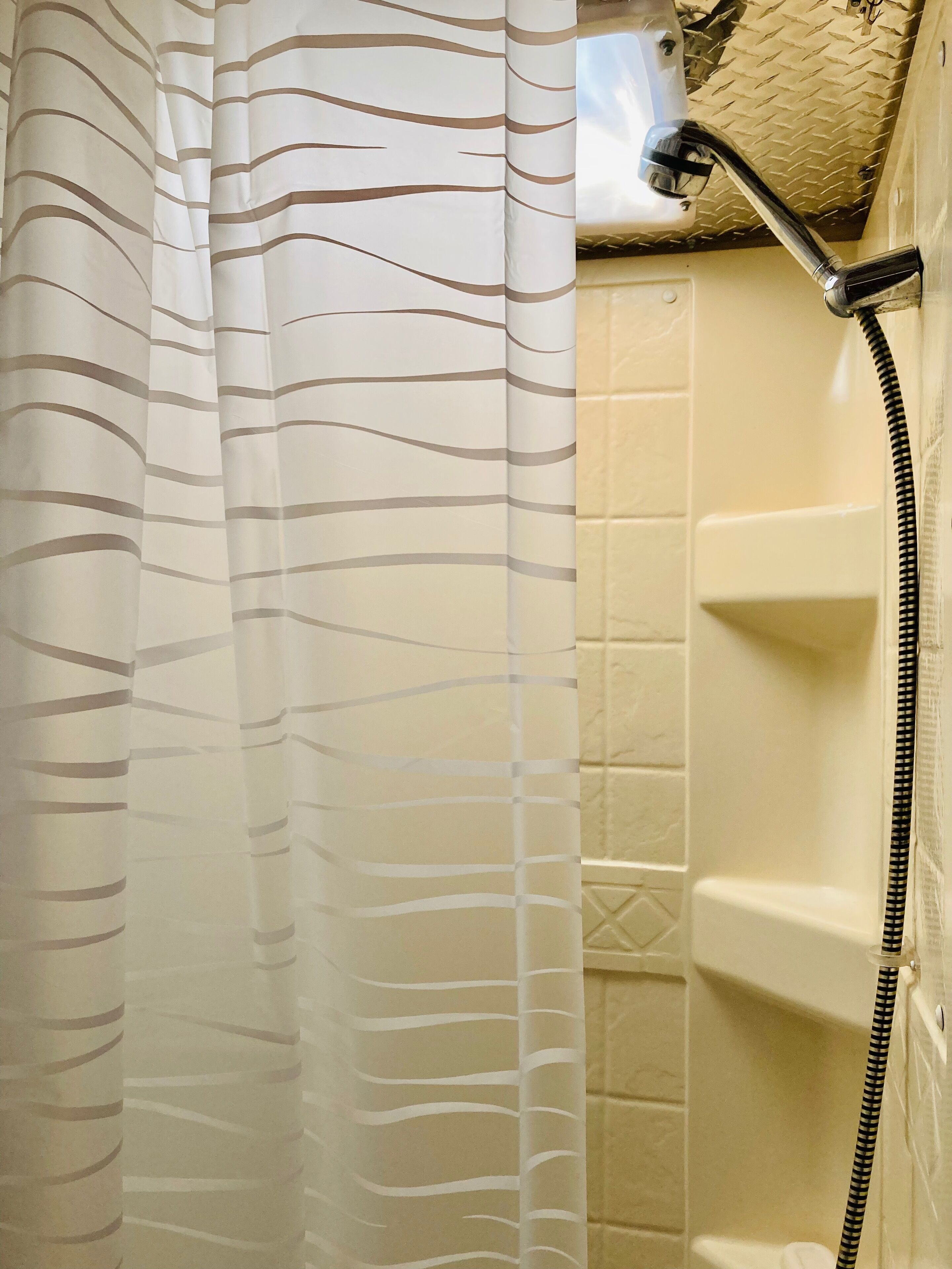 A bathroom with a shower, a white tiled wall, and a striped shower curtain.