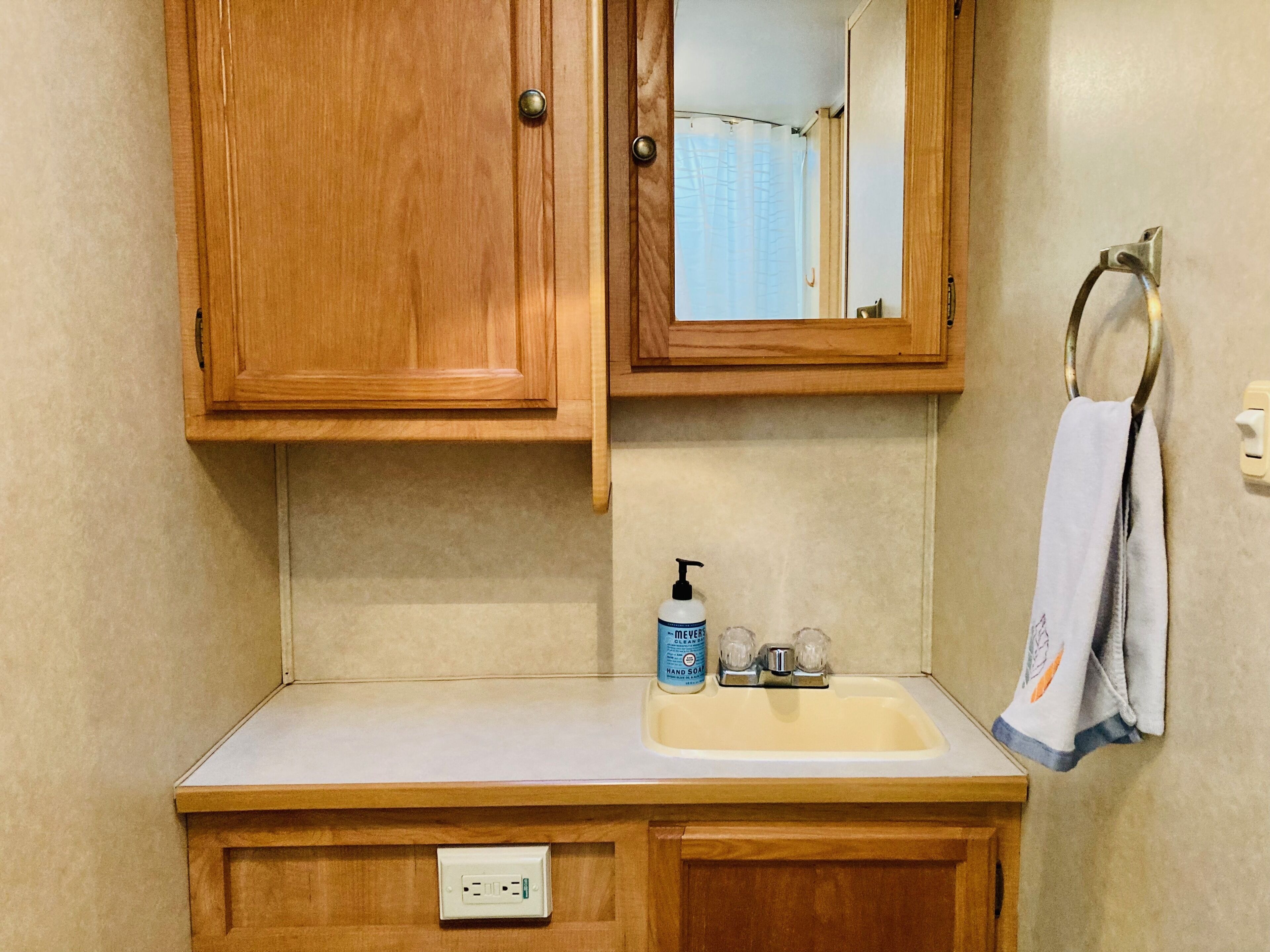 A bathroom with wooden cabinets, a sink with a soap dispenser, and a towel hanging on a metal towel ring.
