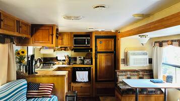 A compact RV kitchen with wooden cabinets, a microwave, a stove, and a sink.