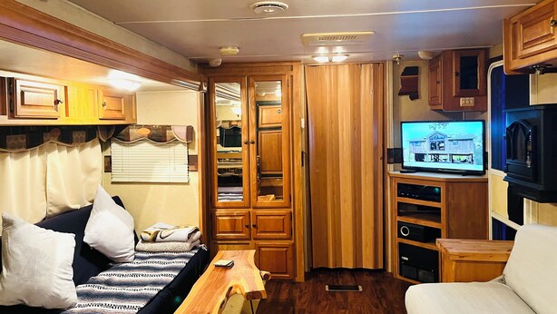A compact RV interior with a bed, a wooden table, a TV, and a microwave.