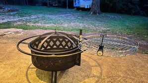 A metal fire pit with a grill and a metal rack, surrounded by a concrete area.
