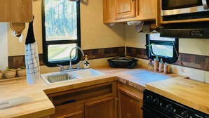 A compact RV kitchen with wooden cabinets, a stove, a microwave, and a sink.