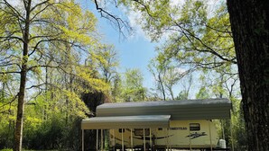 A mobile home with a covered porch, surrounded by trees and a clear sky.