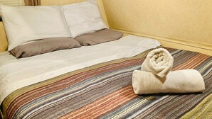 A hotel room with a bed, pillows, a striped bedspread, and a rolled towel.
