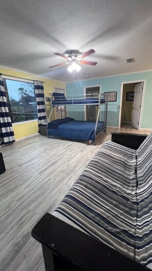 A room with bunk beds, a ceiling fan, a window with curtains, and a striped sofa.