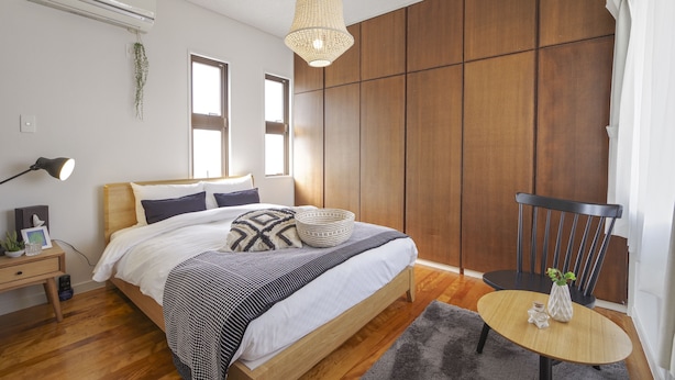 Un dormitorio con cama de madera, mesita de noche, lámpara y una pequeña mesa redonda con un florero.
