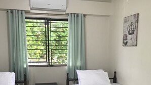 Una habitación con dos camas individuales, una mesita de noche, una ventana con cortinas y un aire acondicionado de pared.
