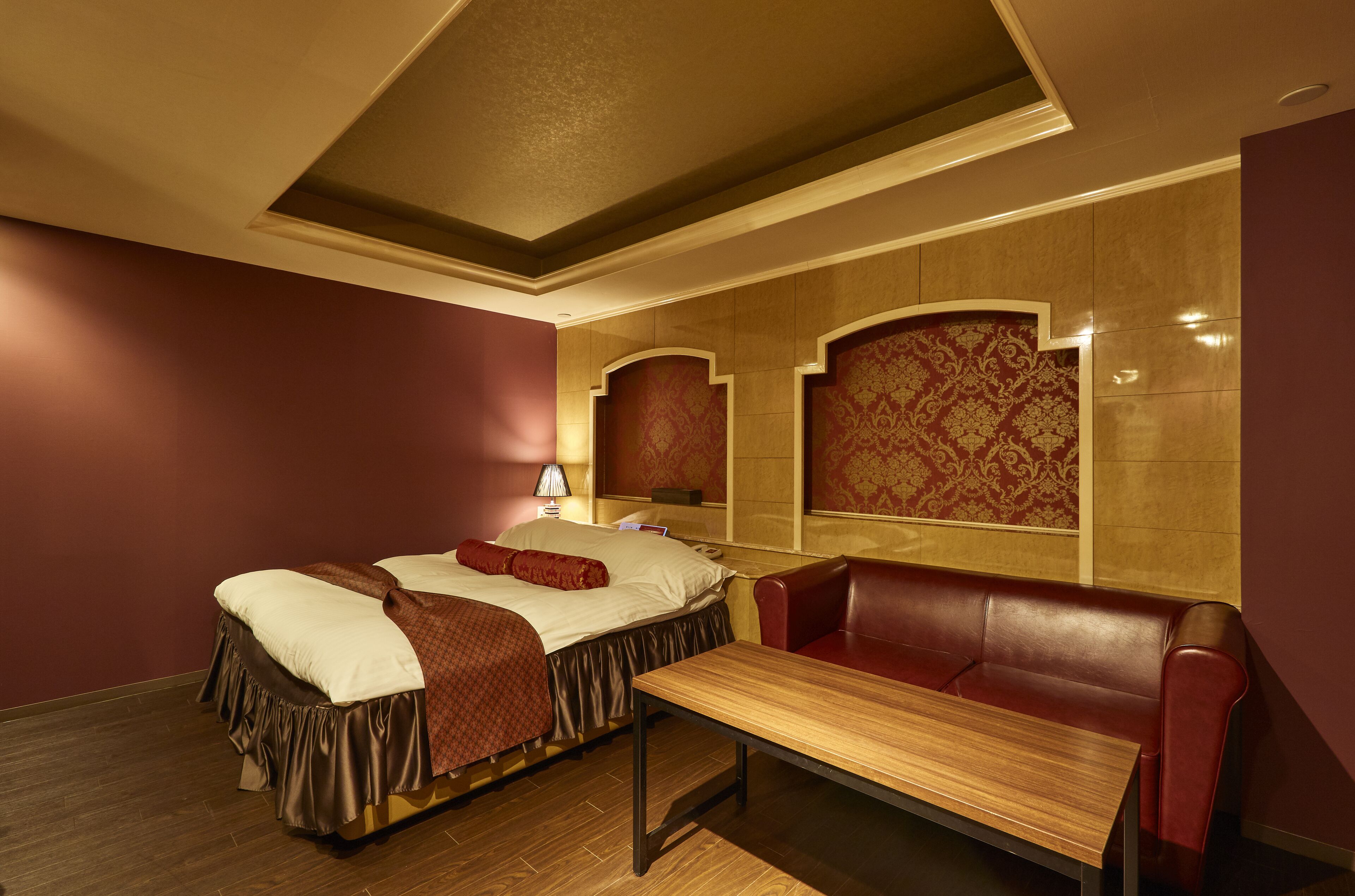 Una habitación de hotel con cama, una mesa de madera, un sofá de cuero rojo y una pared con estampado.