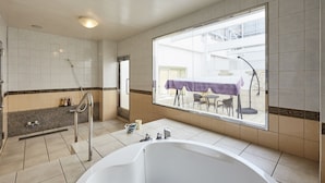A modern bathroom with a large bathtub, a shower, and a window providing a view of an outdoor patio area. - Hotel Christmas (Inazawa)