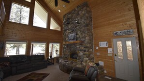 A log cabin interior with a stone fireplace, wooden walls, and large windows. - Limelight Lodge-Waterfront-Boat Dock-WiFi (Fremont County)