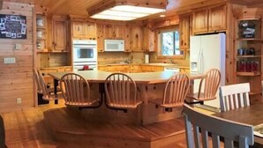 A wooden cabin interior with a kitchen featuring wooden cabinets, a central island with chairs, a refrigerator, and a microwave. - Limelight Lodge-Waterfront-Boat Dock-WiFi (Fremont County)