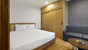 Ein Schlafzimmer mit einem Bett, einem Holzschrank, einem grauen Sofa und einem kleinen Tisch mit einer Zeitschrift.