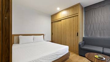 A bedroom with a bed, a wooden wardrobe, a grey sofa, and a small table with a magazine.