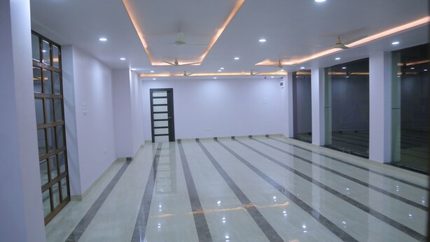 A spacious, well-lit room with a modern design, featuring a large window, a door, and a ceiling fan. - Hotel Saraogi Palace (Gaya)