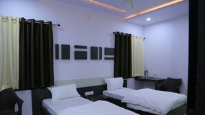 A hotel room with two single beds, a desk, a chair, and a small table with toiletries. - Hotel Saraogi Palace (Gaya)