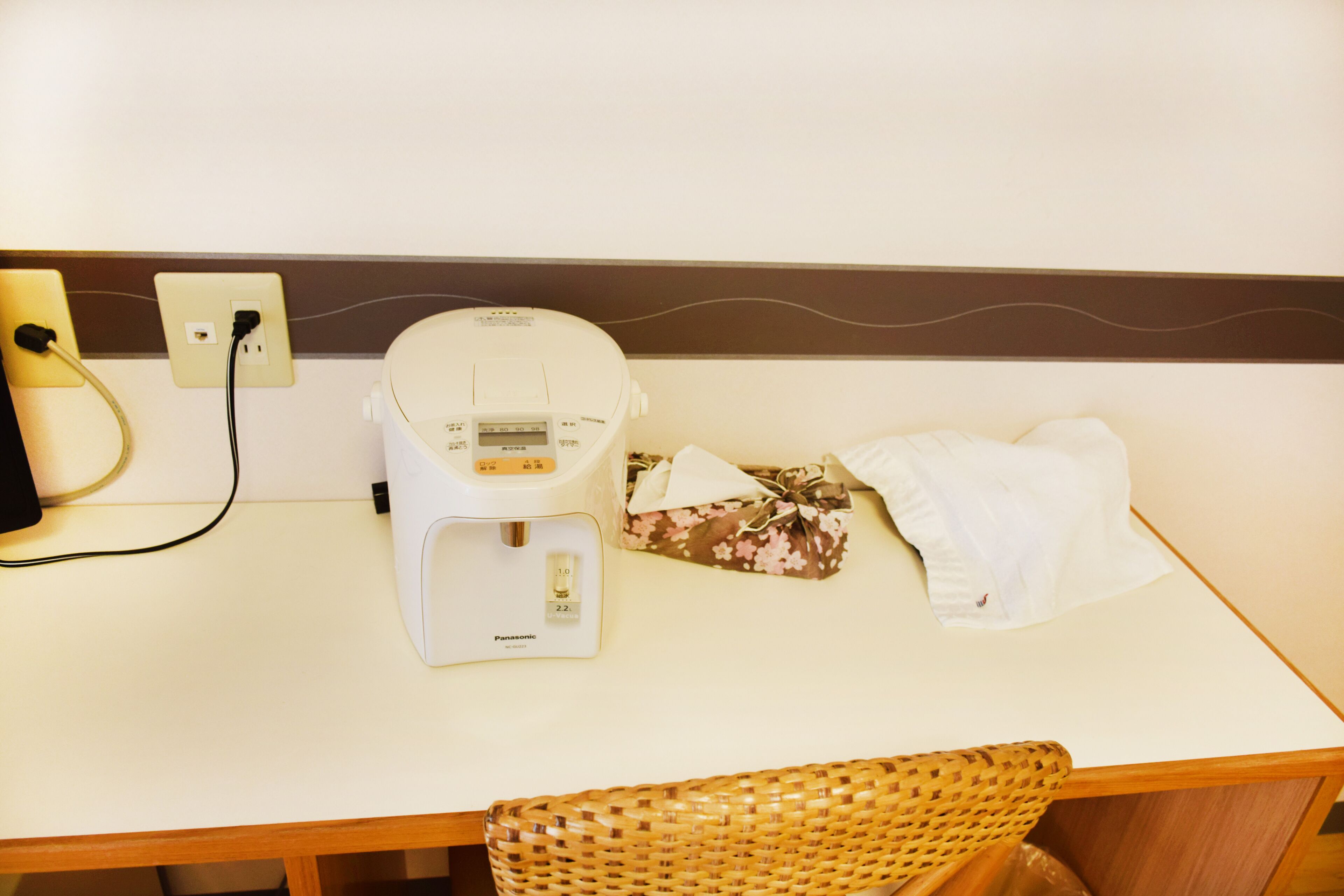 Ein Hotelzimmer mit einem weißen Tisch, einer Panasonic-Kaffeemaschine, einer Blumengeschenkbox und einem weißen Handtuch.