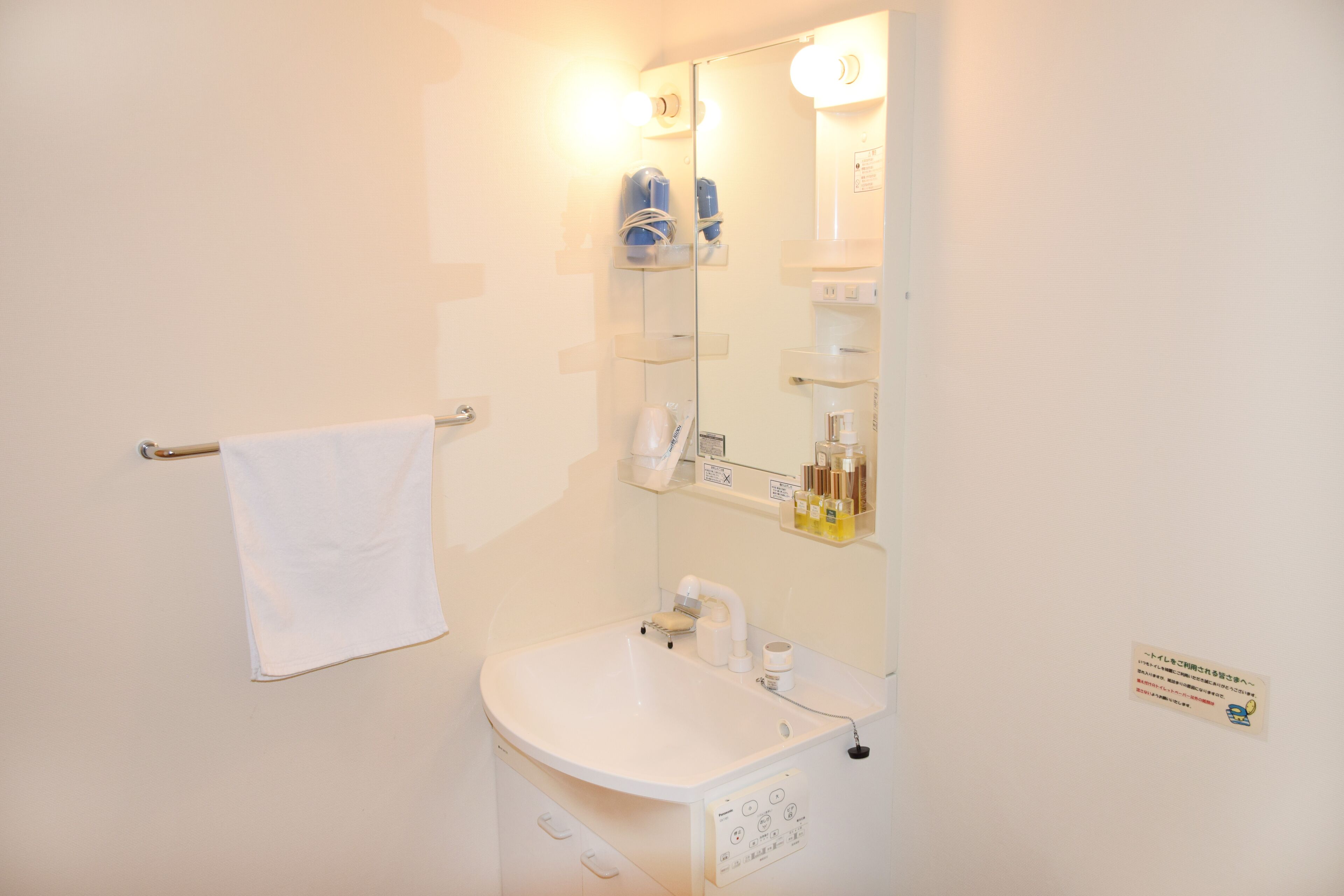 A bathroom with a white sink, a towel rack, a mirror, and shelves with toiletries.