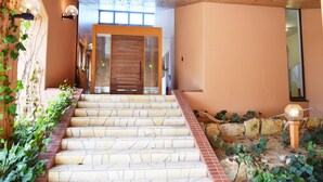Un escalier menant à une porte en bois, entourée de plantes et d’un mur de pierre.