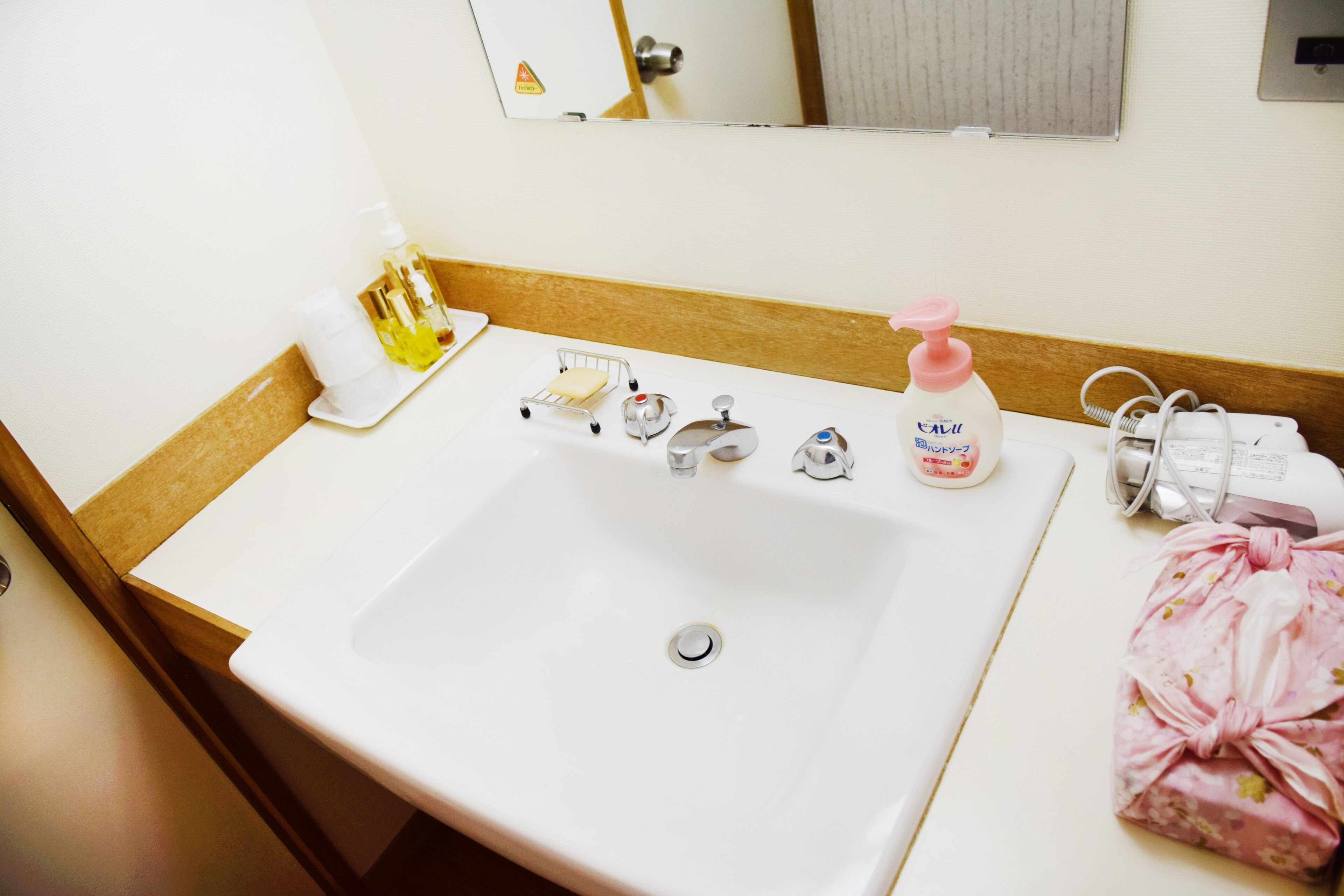 Een hotelbadkamer met een wastafel, meerdere kraanwerkstukken, een spiegel en toiletartikelen.