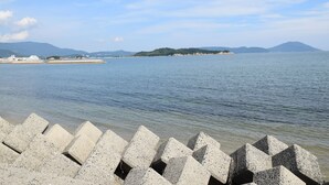 Une vue sur le littoral, avec une digue en béton, des eaux calmes et des montagnes à l’horizon.