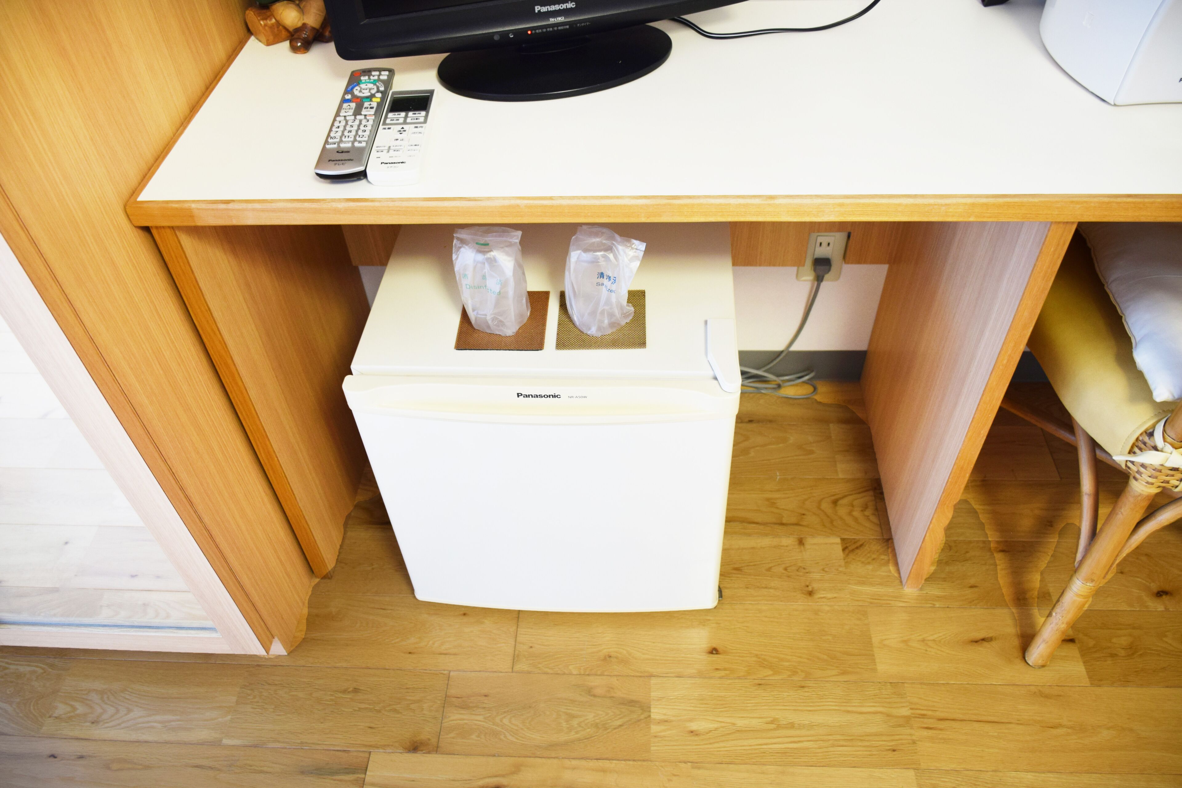 A compact room with a wooden desk, a white refrigerator, and a television on top.