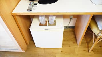 A compact room with a wooden desk, a white refrigerator, and a television on top.