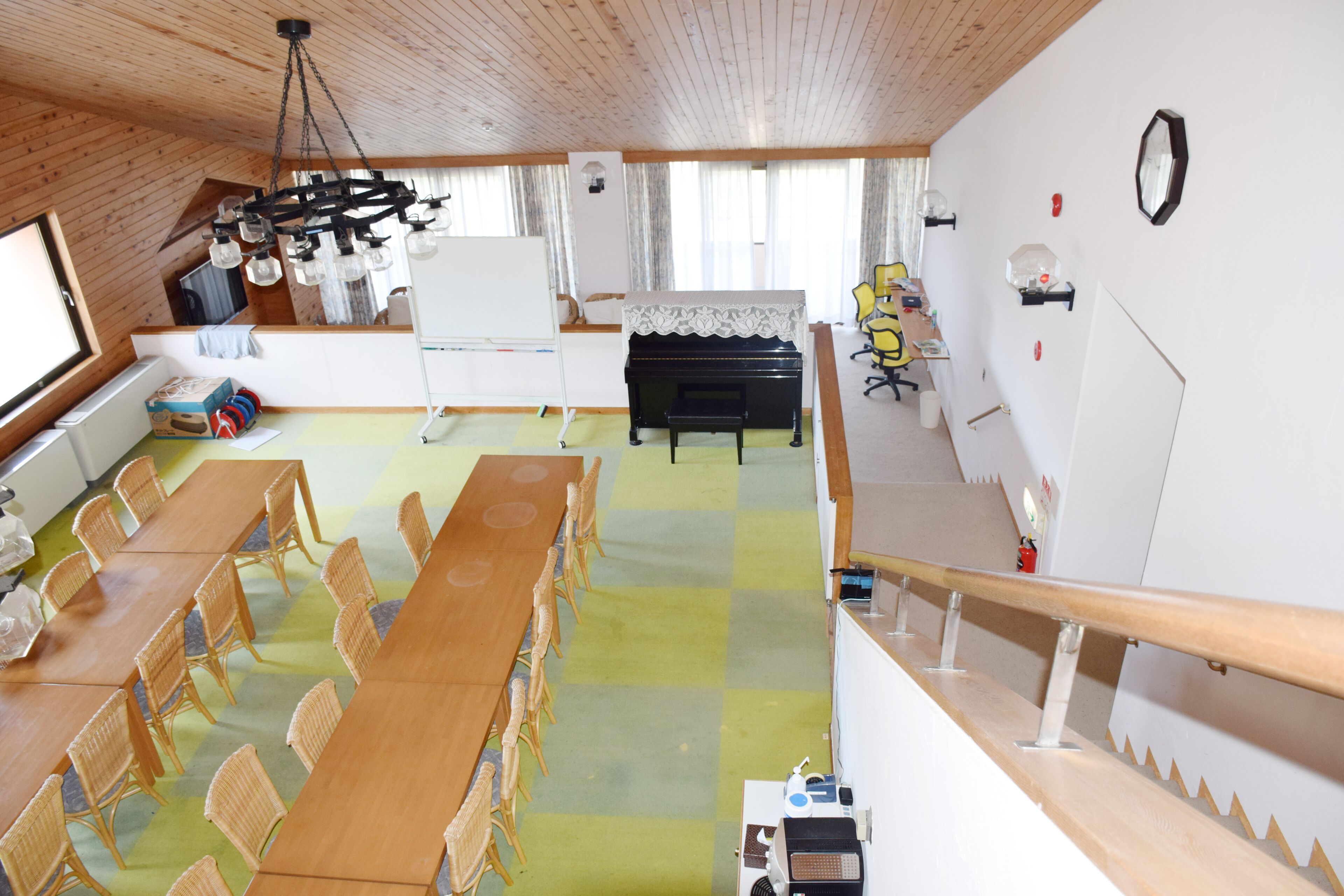 A dining area with a long wooden table and wicker chairs, a piano, and a whiteboard.