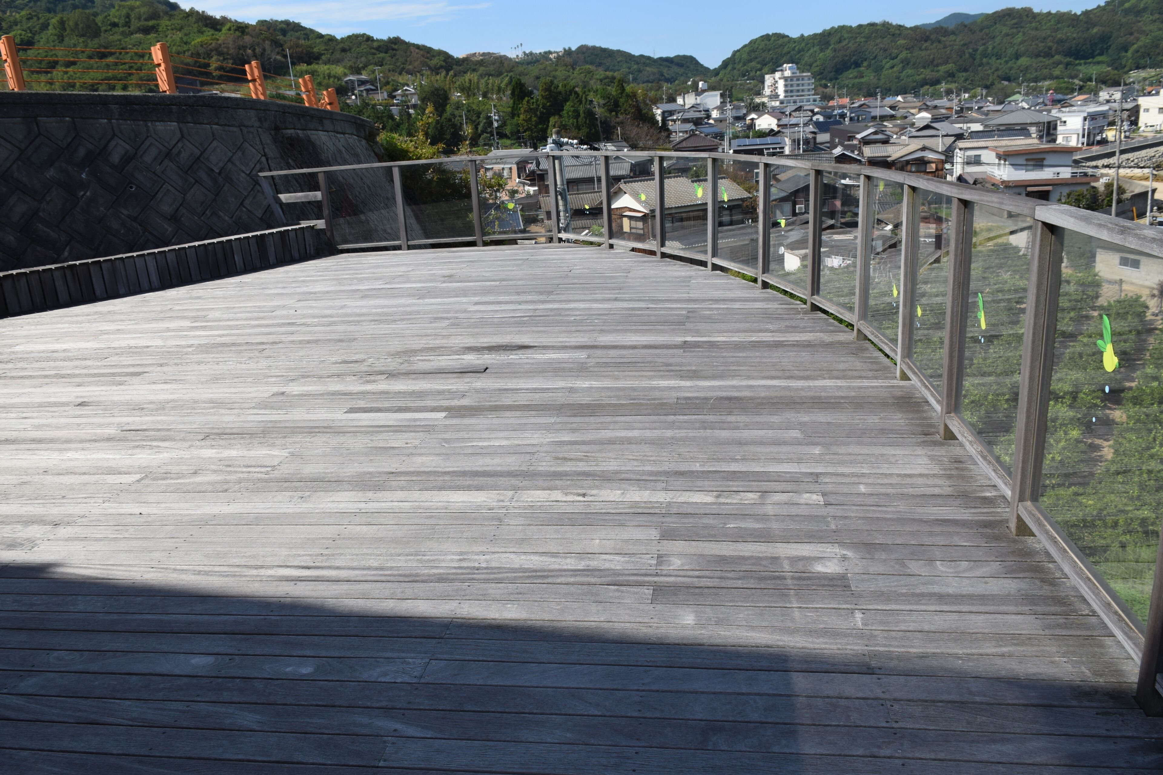 A wooden deck with a glass railing overlooking a town.