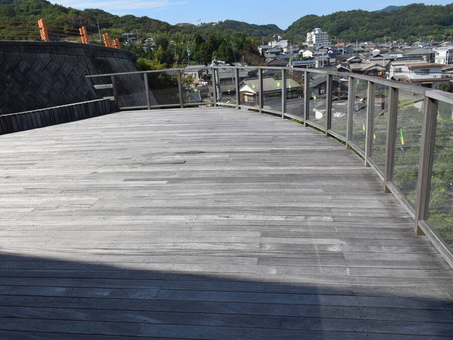 A wooden deck with a glass railing overlooking a town.
