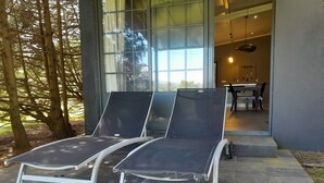 Two lounge chairs outside a building with a glass door, a dining area visible inside, and trees in the background. - Guest House with excellent way for walking, explore neighbor villages or bicycle (Fenais da Luz)