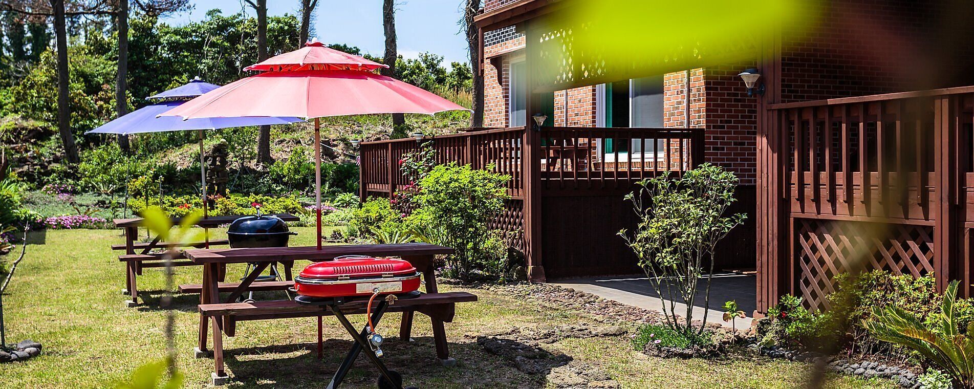 A backyard with picnic tables, barbecue grills, and umbrellas.