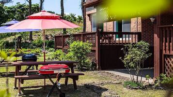 A backyard with picnic tables, barbecue grills, and umbrellas.