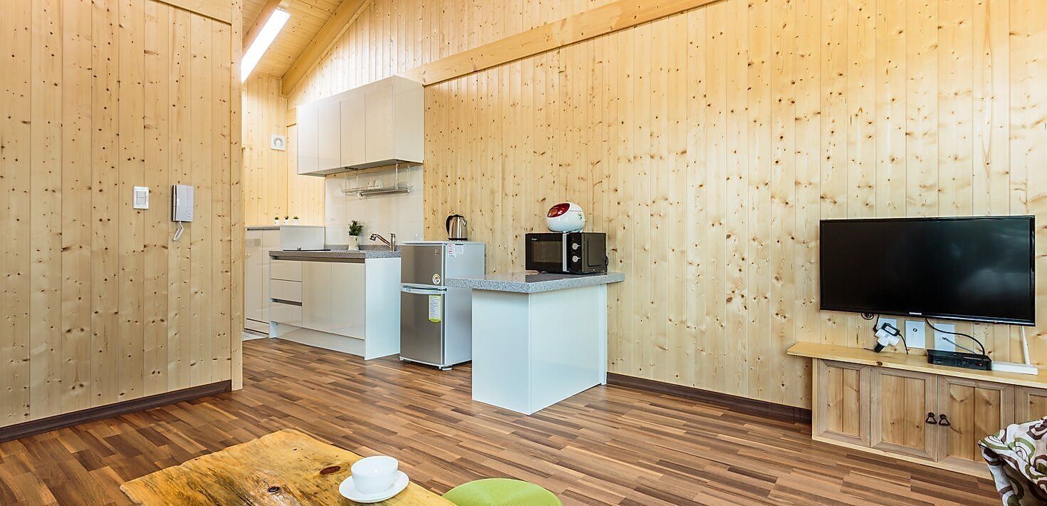 Cocina compacta con armarios blancos, microondas y televisor sobre un mueble de madera.