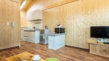 Cocina compacta con armarios blancos, microondas y televisor sobre un mueble de madera.