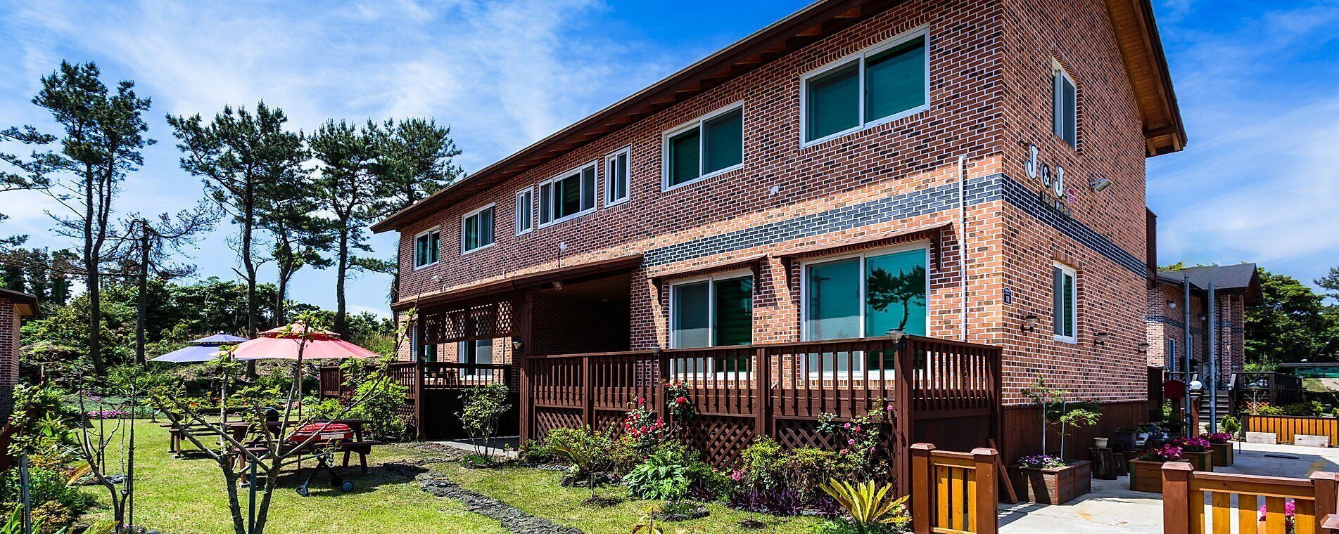 A two-story brick building with a covered patio area, a wooden deck, and a garden with various plants and a barbecue setup.