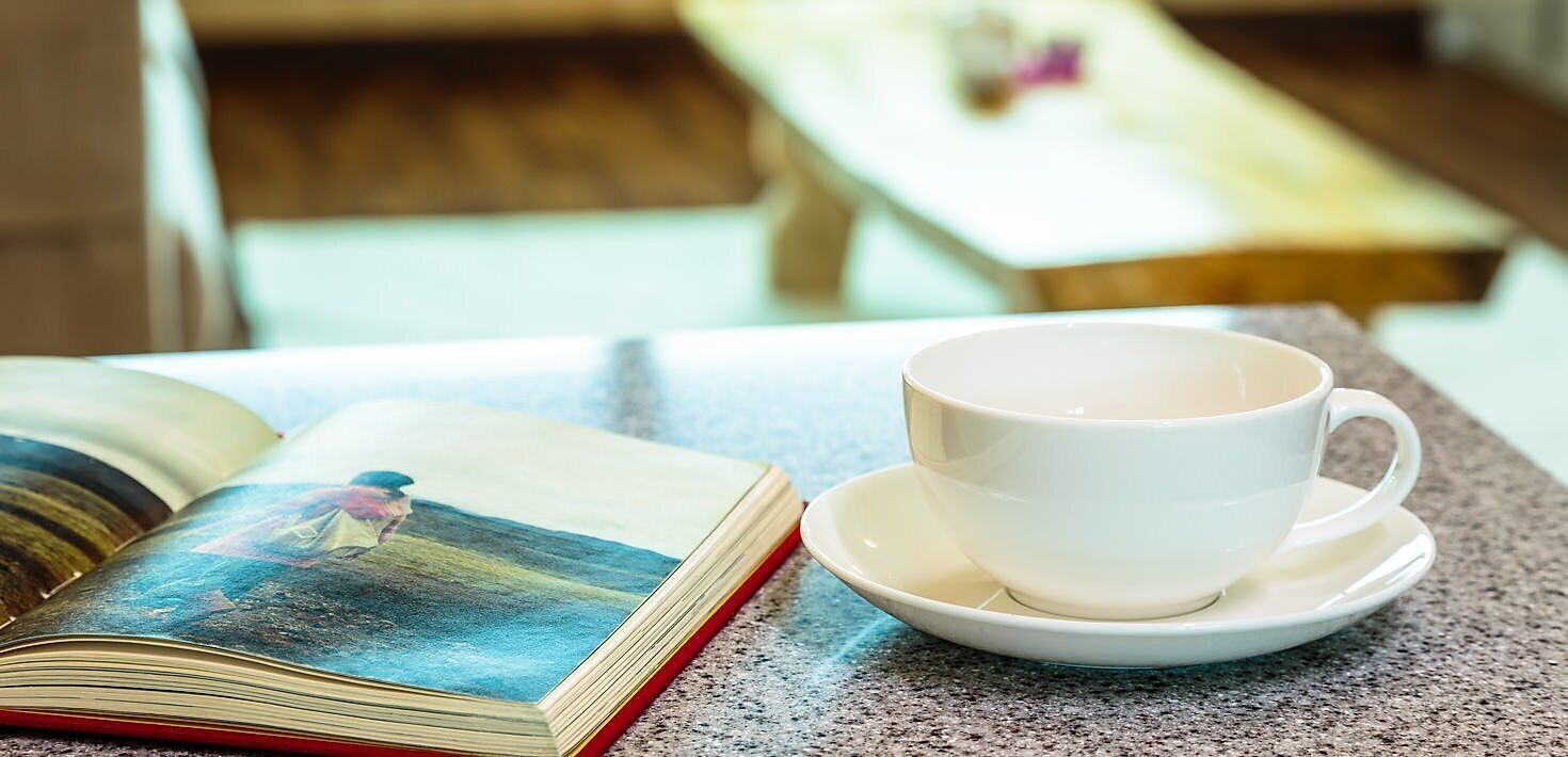 Un libro abierto con una fotografía sobre una mesa, una taza y platillo blancos, y un fondo desenfocado.