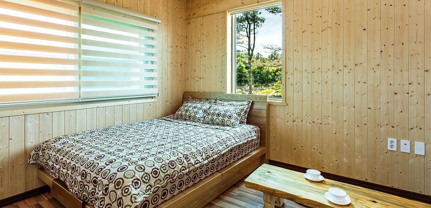 A wooden-paneled room with a bed, a window, and a small table with cups.