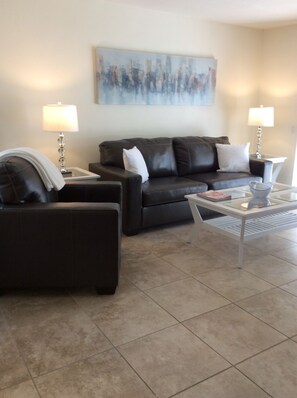 A living room with a dark leather sofa, a glass coffee table, and two lamps. - Beautiful Condo at Mesquite Country Club -Pool, Hot Tub, Tennis (City ID:4337) (Palm Springs)