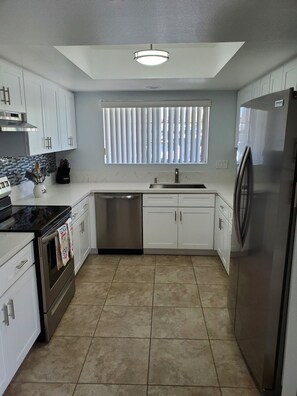 A modern kitchen with white cabinets, a stainless steel refrigerator, a black stove, and a window with blinds. - Beautiful Condo at Mesquite Country Club -Pool, Hot Tub, Tennis (City ID:4337) (Palm Springs)